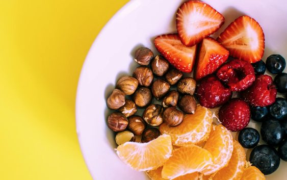 Close-up of a bowl with fresh fruits and nuts against a vibrant yellow backdrop.